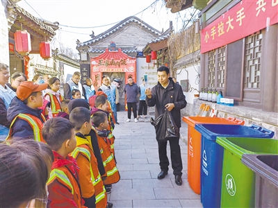 图为环卫工作人员向小志愿者讲解分类垃圾桶功能。张志忠摄