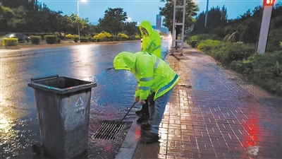图为市政工人冒雨清理下水篦上的杂物。高雅敏摄